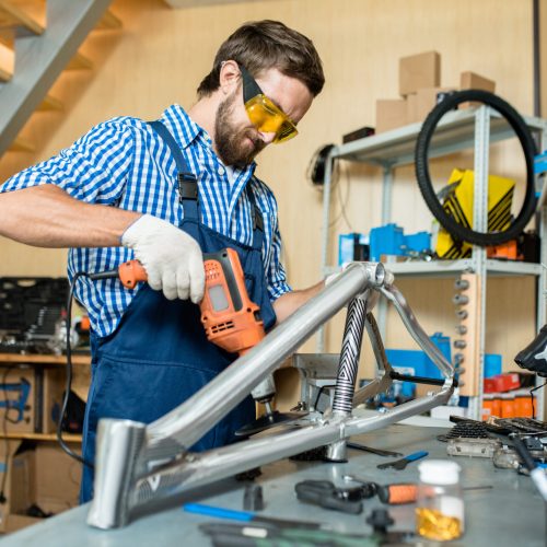 Repairman working with electric drill by workplace in his own workshop